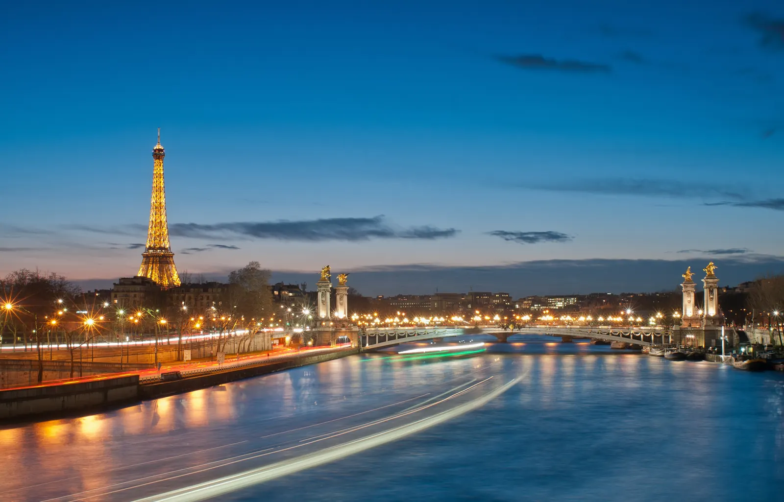 The Eiffel Tower and Pont Alexandre III lit up above the Seine at blue hour